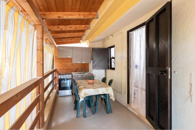 Tavolo con sedie in terrazza coperta, cucina sul fondo.