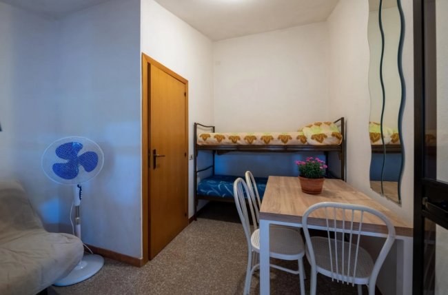 Letto a castello, tavolo con sedie, ventilatore e divano.