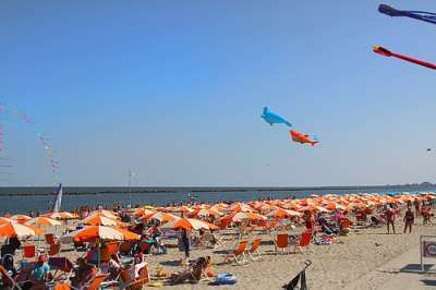 Spiaggia con ombrelloni arancioni e aquiloni colorati nel cielo.