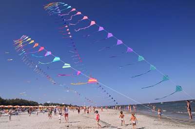 Spiaggia affollata con aquiloni multicolori volanti nel cielo azzurro.