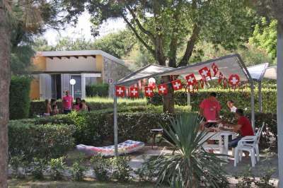 Alcune persone sono sedute sotto un gazebo decorato con bandierine, circondato da alberi e cespugli.