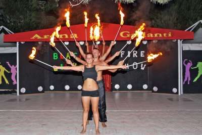 Due artisti di fronte a un palco, ognuno con fiamme in mano, durante uno spettacolo di fuoco serale.