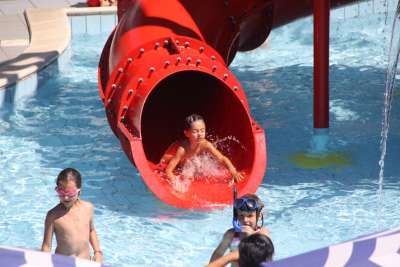Bambini che giocano su uno scivolo d’acqua rosso in piscina.
