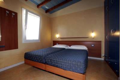 Camera con due letti singoli, pareti beige, luci soffuse e soffitto con travi in legno.