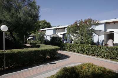 Giardino con sentieri e arbusti, accanto a case bianche con tetti spioventi.