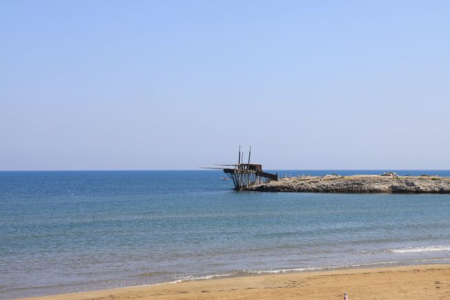 Spiaggia sabbiosa con mare calmo e struttura di legno sul promontorio.