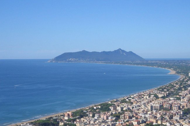 Vista aerea di una costa con spiaggia e montagna in lontananza.