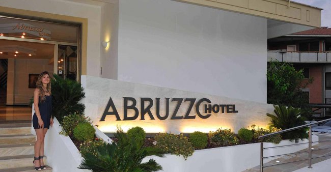 Ingresso di un hotel con una donna accanto al cartello Abruzzo Hotel.