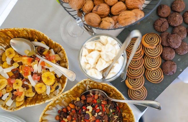Vassoi di frutta secca, banane, noci e biscotti assortiti su un tavolo.
