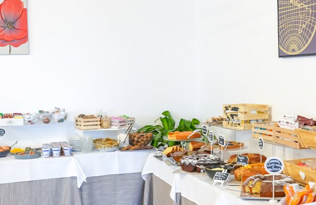 Tavolo buffet con torte, frutta e dolci vari su tovaglie bianche.