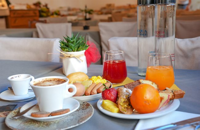 Colazione con caffè, succhi, frutta e dolci su un tavolo apparecchiato.