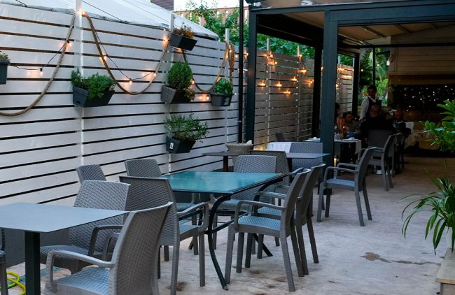 Patio con tavoli, sedie e luci decorative sulle pareti.