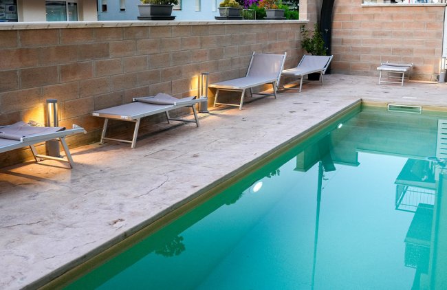 Area piscina con lettini e luci soffuse lungo il bordo.