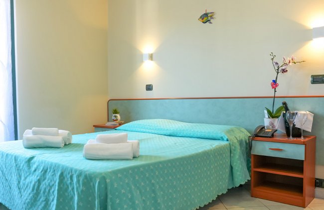 Camera con letto matrimoniale, lenzuola azzurre, telefono e asciugamani.