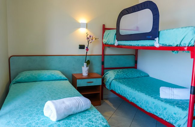 Una camera con letto singolo e letto a castello, copriletti azzurri e asciugamani bianchi.