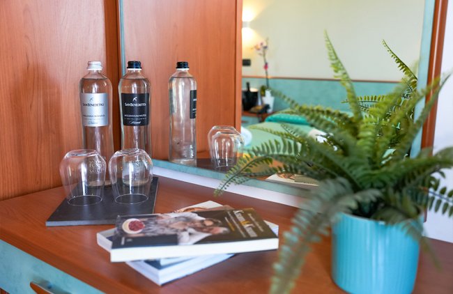 Una scrivania con libri, bottiglie d'acqua, bicchieri e una pianta in vaso verde.