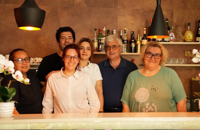 Sei persone sorridenti davanti a un bancone con bottiglie sullo sfondo.