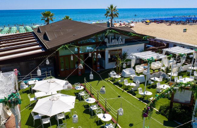 Locale sulla spiaggia con sedie, tavoli, ombrelloni e vista mare.