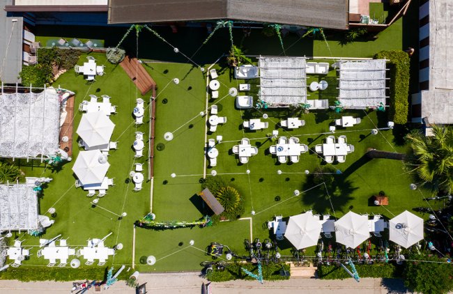 Cortile con tavoli bianchi e pergolati su prato verde.