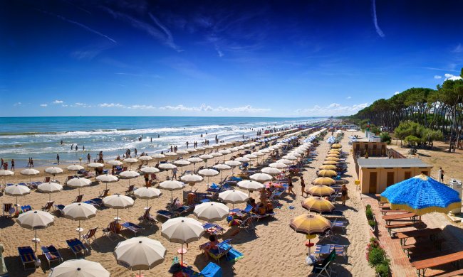 Una spiaggia affollata con ombrelloni e lettini allineati lungo la costa.