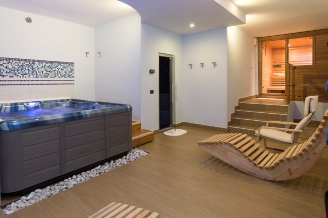 Una spa interna con vasca idromassaggio, lettini in legno e sauna.