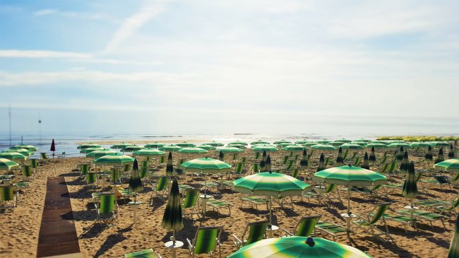 Spiaggia con ombrelloni verdi e lettini su sabbia dorata, cielo sereno.
