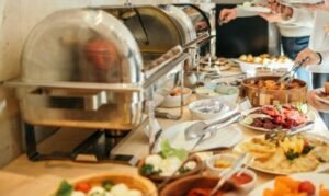 Buffet con piatti vari, persone che si servono cibo.