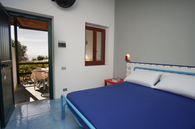 Camera da letto con letto blu e terrazza con vista mare.