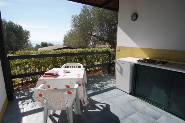 Terrazza con tavolo bianco e vista su alberi e mare.