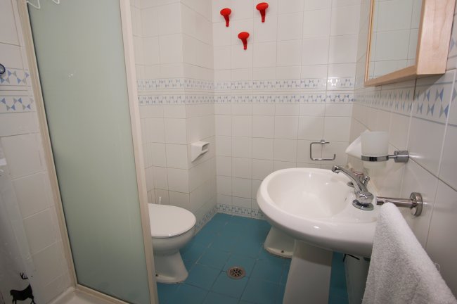 Bagno con piastrelle bianche, lavandino e box doccia.
