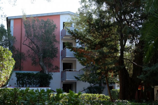 Edificio con parete rosa tra alberi verdi.