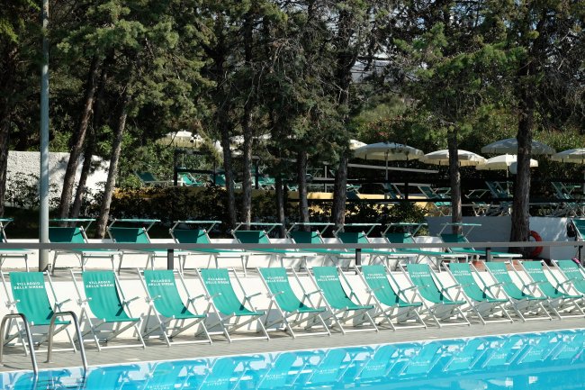 Lettini verdi a bordo piscina con ombrelloni.