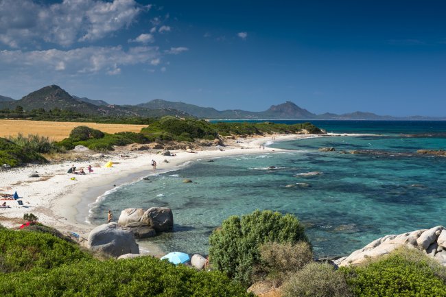 Spiaggia con acqua cristallina e montagne sullo sfondo.