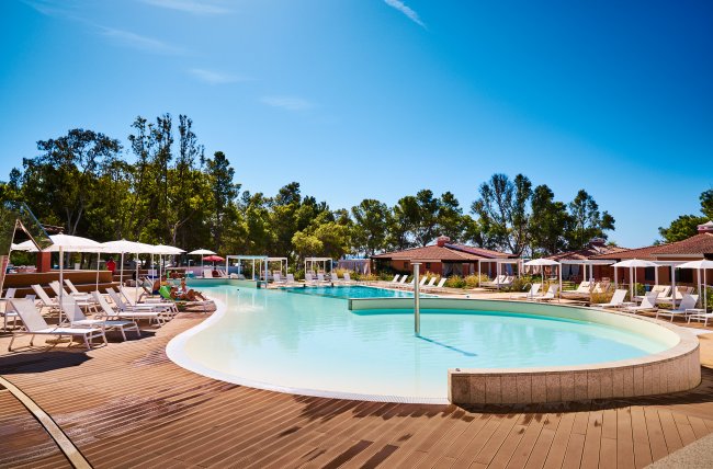 Piscina rotonda con sedie a sdraio e alberi sullo sfondo.