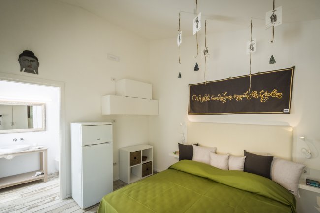Stanza luminosa con letto verde e mobile bianco.