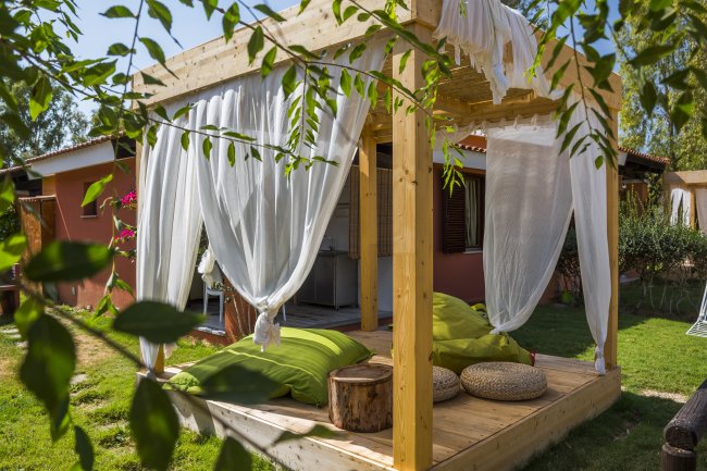 Pergola in legno con tende bianche e cuscini verdi.
