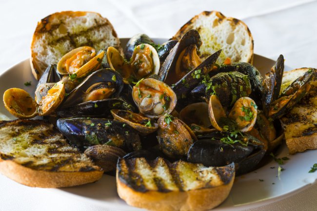 Cozze e vongole con crostini su un piatto bianco.