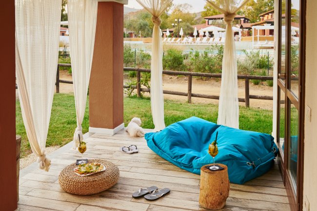 Terrazza con tenda, pouf blu e vista piscina.