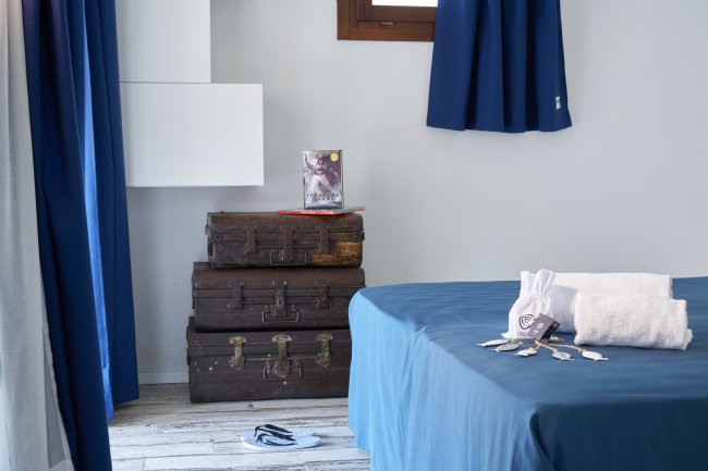 Valigie vintage accanto a un letto su pavimento in legno chiaro.