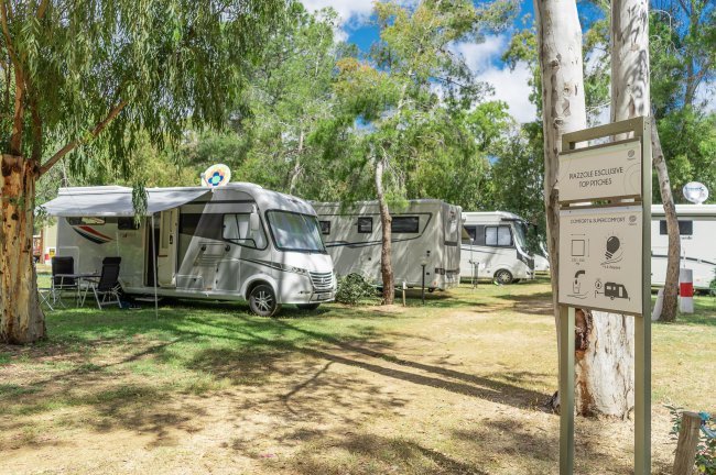 Camper parcheggiati in un'area ombreggiata da alberi.