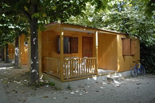 Bungalow in legno con veranda, circondato da alberi ombrosi e una bicicletta parcheggiata.