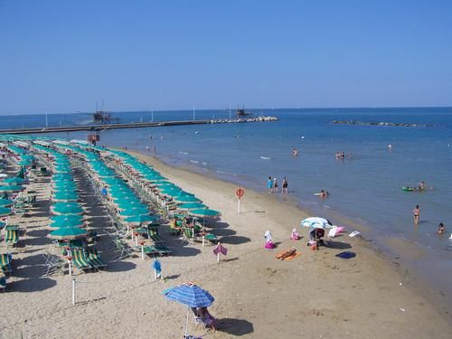 Spiaggia con file di ombrelloni verdi e persone che nuotano nel mare.