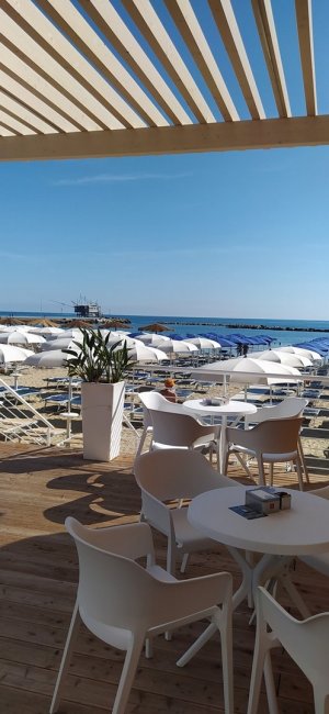 Terrazza con tavoli bianchi e vista mare soleggiata.