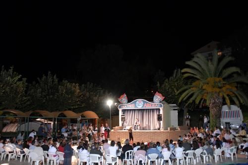 Spettacolo serale all'aperto con pubblico seduto davanti a un palco.