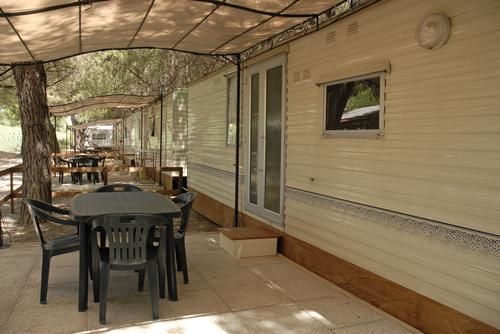 Esterno di una roulotte attrezzata con tavolini e sedie sotto un tendalino.