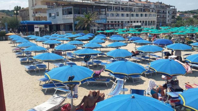 Ombrelloni blu su una spiaggia sabbiosa con edifici sullo sfondo.