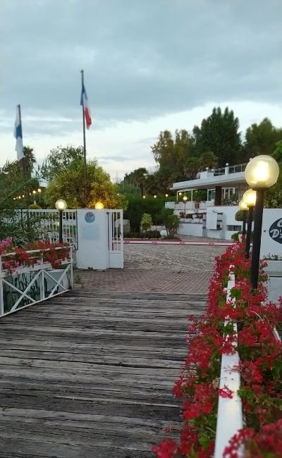 Sentiero di legno con fiori rossi e luci verso un edificio bianco.
