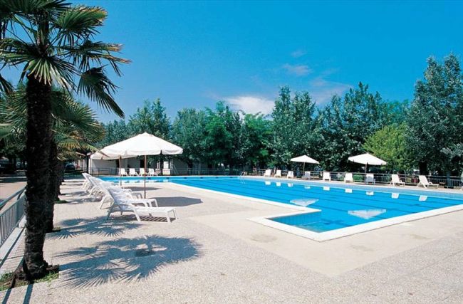 Piscina vuota con lettini bianchi e palme.