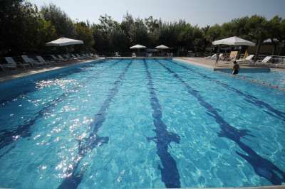 Piscina vuota con strisce blu sul fondo, circondata da ombrelloni e lettini.