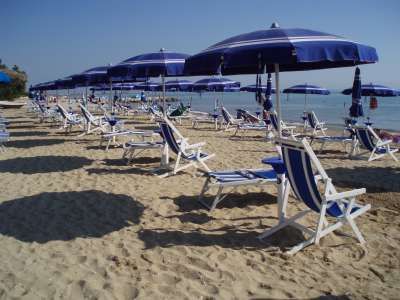 Lettini e ombrelloni blu su una spiaggia sabbiosa sotto un cielo sereno.
